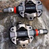 Two bicycle pedals with 'Favero' branding on a stone surface