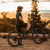 Person on a mountain bike overlooking a scenic landscape with trees and mountains at sunset.