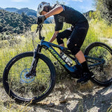 Person riding a mountain bike on a trail with greenery and mountains in the background