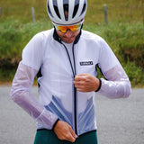 Person wearing a white cycling jacket with a brand logo, helmet, and sunglasses on a road.