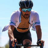 Cyclist in a white jersey with blue accents riding a bicycle on a clear day.