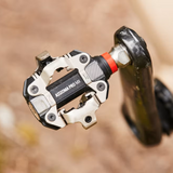 Close-up of a bicycle pedal with 'KMC' branding on a blurred natural background