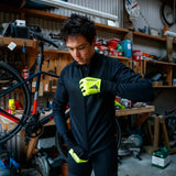Person in a workshop adjusting a bicycle, wearing a black jacket and yellow gloves.