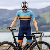 A man wearing a navy blue, orange, and black road runner jersey with a matching bicycle helmet, standing next to a black bicycle.