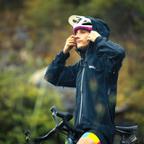 Person wearing a dark raincoat and helmet, sitting on a bicycle with a blurred natural background
